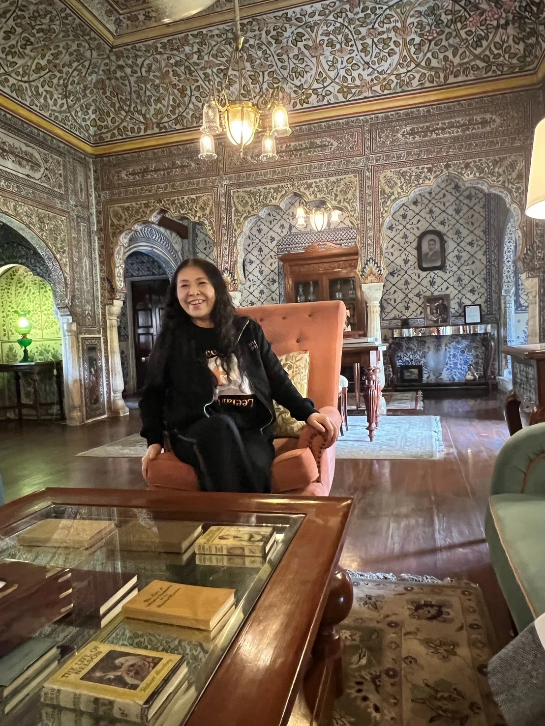 鏡や花模様で飾られた部屋で、椅子に座って笑う巡礼者。